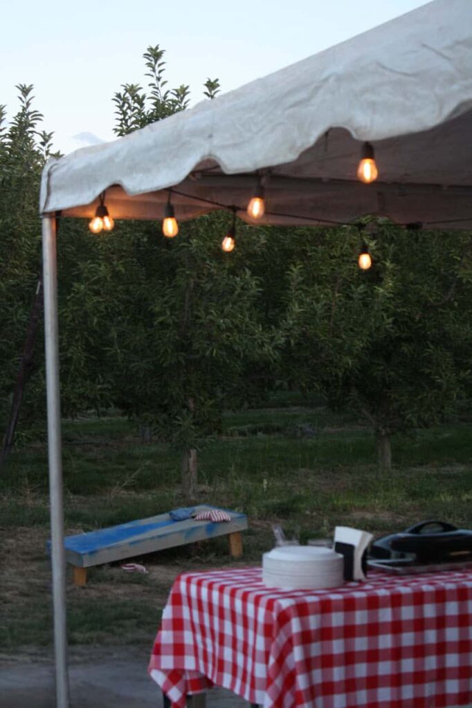 White tent with table and corn hole game with lights hanging.